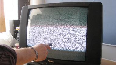 Kuvassa vanhan mallinen televisio, josta näkyy "lumisadetta". Kuvassa vasemmalla ihmisen kädessä oleva kaukosäädin.